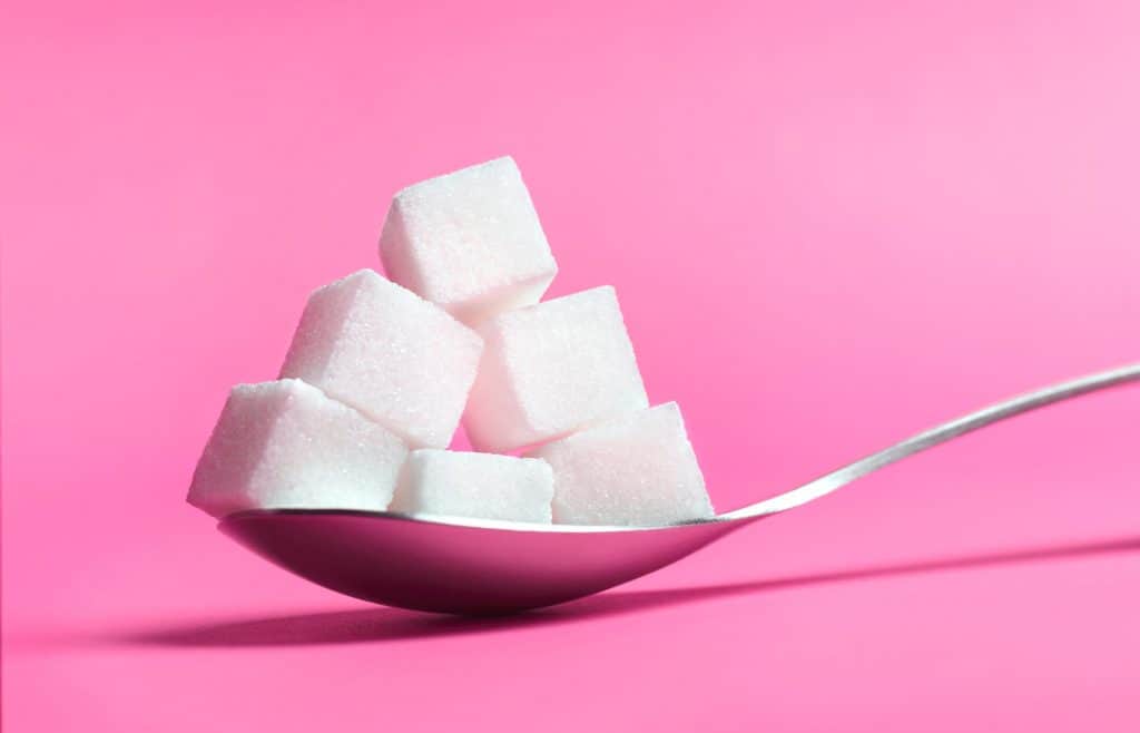 Kostki cukru na łyżce i różowym tle